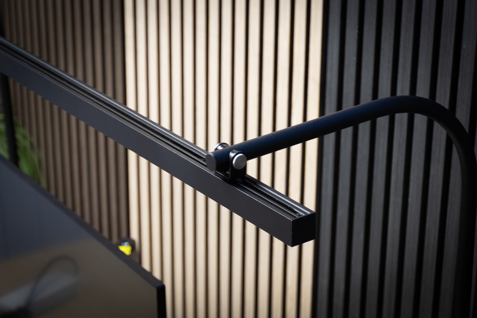 Close-up of the LightEFX Shift desk light aluminium arm profile and hinge connection against acoustic slat panelling
